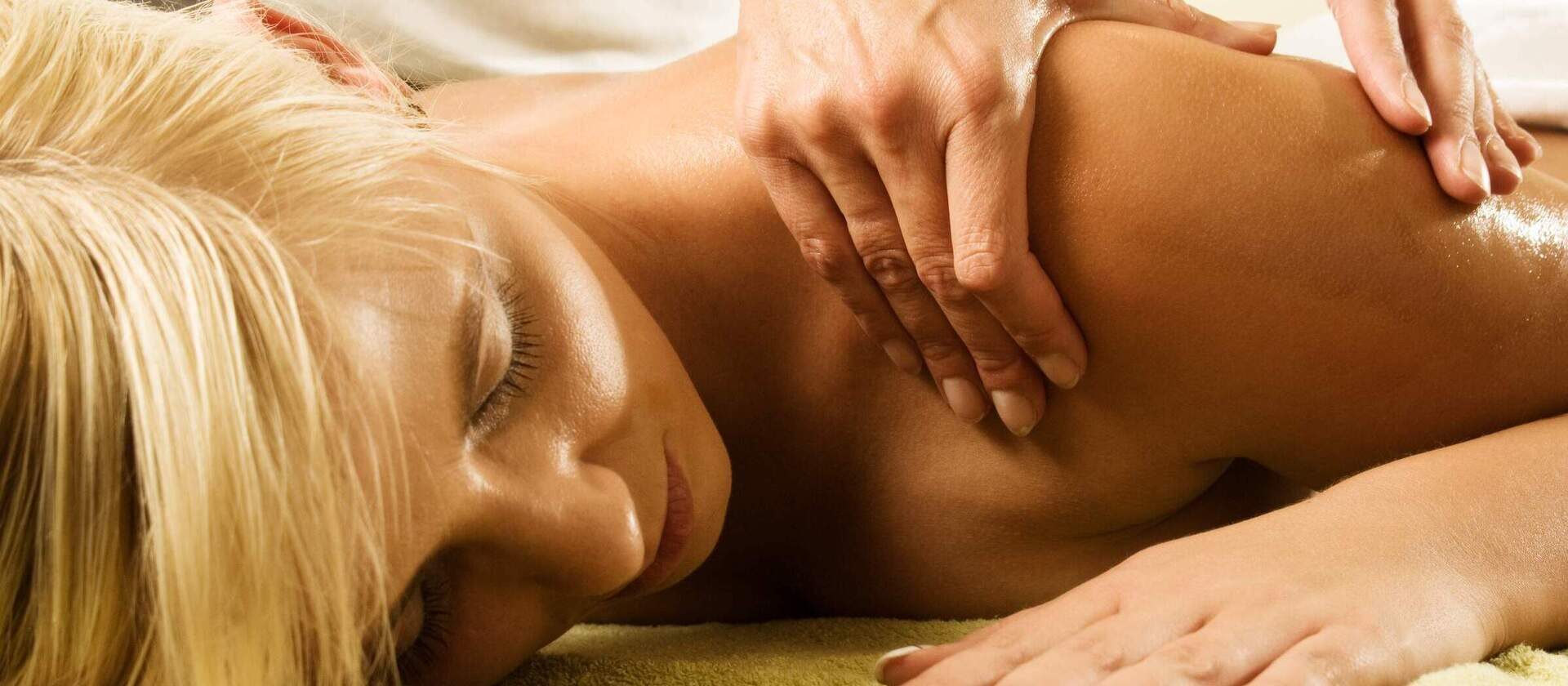 Nahaufnahme einer auf dem Bauch liegenden Frau die eine Rückenmassage im Hotel Happinger Hof in Rosenheim erhält.