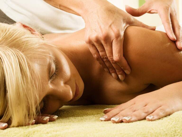 Nahaufnahme einer auf dem Bauch liegenden Frau die eine Rückenmassage im Hotel Happinger Hof in Rosenheim erhält.